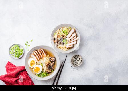 Hühnerramen-Nudeln in einer Schüssel auf grauer Betonkulisse. Tabellenansicht von oben. Asiatische Küche Stockfoto