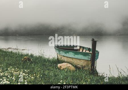 Nahaufnahme einer Filmaufnahme von trüben nebligen Landschaften am Morgen auf dem Flussufer mit einem Fischerboot. Stockfoto