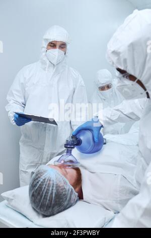 Mann, der während der Operation im Operationssaal mit Sauerstoffmaske liegt Mit Chirurgen Stockfoto