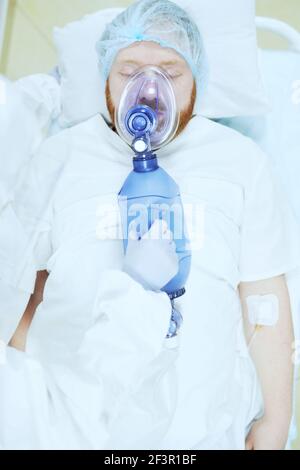 Hochwinkelansicht des männlichen Patienten in der Sauerstoffmaske liegend Auf dem Bett während des Betriebs im Operationssaal Stockfoto
