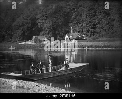 CLIVEDEN FERRY, Cliveden, Taplow, Buckinghamshire. Der Fährmann ist bereit, zwei Männer und einen Jungen über den Fluss zu bringen. Der Mann saß auf der Seite des Stockfoto