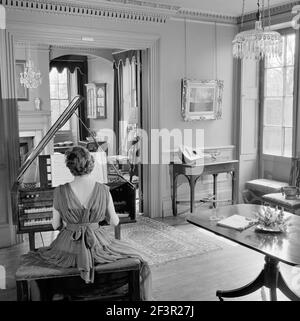 FENTON HOUSE, Hampstead, London. Innenansicht mit einer Frau in Abendkleid, die das Cembalo spielt. Fotografiert von John Gay. Datumsbereich: 1960 Stockfoto
