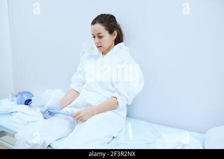 Ärztin in Uniform sitzt auf dem Bett im Operationssaal Stockfoto