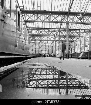 CHARING CROSS STATION, LONDON. Menschen, die neben einem stillstehenden Zug auf Bahnsteig 4 mit dem Bahnhofsdach in einer Pfütze im Vordergrund gehen. Stockfoto