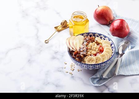 Haferbrei mit karamellisierten Äpfeln mit Zimt, Banane, geriebenen Erdbeeren und Honig auf hellem Marmorboden Stockfoto