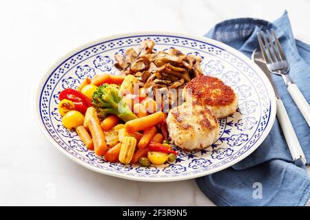 Gemischtes Gemüse aus Karotten, Brokkoli, Babykorn, Paprika, gerösteten Champignons und zwei Hühnerpasteten in Paniermehl Stockfoto