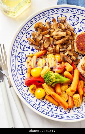 Gemischtes Gemüse aus Karotten, Brokkoli, Babykorn, Paprika, gerösteten Champignons und zwei Hühnerpasteten in Paniermehl Stockfoto