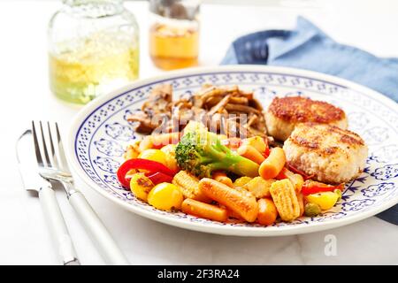 Gemischtes Gemüse aus Karotten, Brokkoli, Babykorn, Paprika, gerösteten Champignons und zwei Hühnerpasteten in Paniermehl Stockfoto