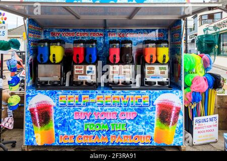 Ein Stall, der eiskalten Slush an der Küste serviert, sowie Fischernetze und andere Strandspielzeug, Westward Ho!, Devon, UK Stockfoto