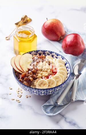 Haferbrei mit karamellisierten Äpfeln mit Zimt, Banane, geriebenen Erdbeeren und Honig auf hellem Marmorhintergrund, Nahaufnahme Stockfoto