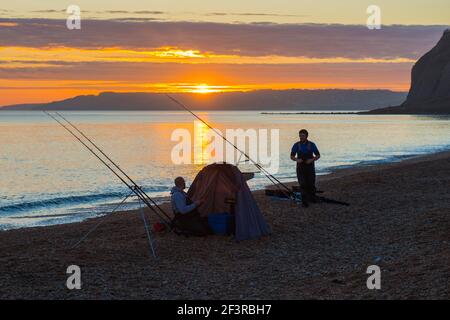 Seatown, Dorset, Großbritannien. 17th. März 2021. Wetter in Großbritannien. Zwei Fischer, die den spektakulären Sonnenuntergang vom Strand aus betrachten, während sich die Wolken beim Sonnenuntergang in Seatown in Dorset rot färben, während der Himmel nach einem bewölkten Nachmittag während der Covid-19-Sperre aufklärt. Bild: Graham Hunt/Alamy Live News Stockfoto