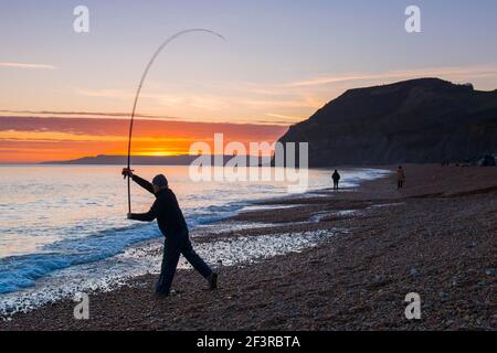 Seatown, Dorset, Großbritannien. 17th. März 2021. Wetter in Großbritannien. Ein Fischer genießt die Seeluft, als er seine Rute am Strand wirft, während die Wolken bei Sonnenuntergang in Seatown in Dorset rot werden, während der Himmel nach einem bewölkten Nachmittag während der Covid-19-Sperre aufklärt. Bild: Graham Hunt/Alamy Live News Stockfoto