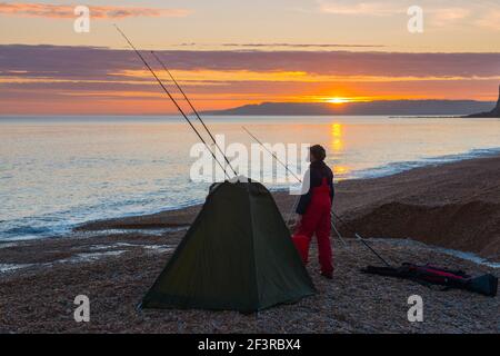 Seatown, Dorset, Großbritannien. 17th. März 2021. Wetter in Großbritannien. Ein Fischer genießt die Meeresluft am Strand, während die Wolken bei Sonnenuntergang am Seatown in Dorset rot werden, während der Himmel nach einem bewölkten Nachmittag während der Covid-19-Sperre aufklärt. Bild: Graham Hunt/Alamy Live News Stockfoto