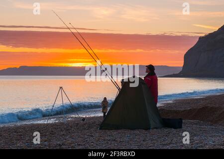 Seatown, Dorset, Großbritannien. 17th. März 2021. Wetter in Großbritannien. Ein Fischer, der die Meeresluft am Strand genießt, während sich die Wolken bei Sonnenuntergang am Seatown in Dorset rot färben, während der Himmel nach einem bewölkten Nachmittag während der Covid-19-Sperre aufklärt. Bild: Graham Hunt/Alamy Live News Stockfoto