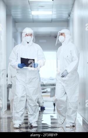 Gruppe von Ärzten in Schutzanzug zu Fuß entlang des Korridors Im Krankenhaus und im Gespräch miteinander Stockfoto