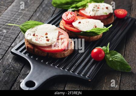 Offene Sandwiches oder Bruschetta mit Mozzarella-Käse, Tomaten und Basilikum, Caprese auf dunklem Holzhintergrund. Stockfoto