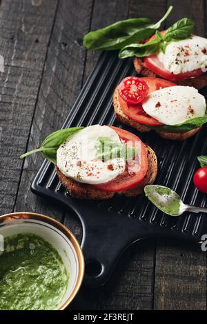 Offene Sandwiches oder Bruschetta mit Mozzarella-Käse, Tomaten und Basilikum, Caprese auf dunklem Holzhintergrund. Stockfoto