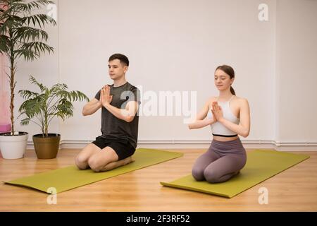 Junges Paar, das gemeinsam Yoga praktiziert, zu Hause in einem modernen Interieur. Hobby, Zweisamkeit, gesunder Lebensstil Stockfoto