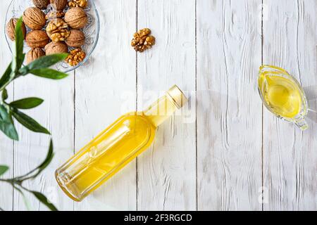 Walnussöl und ein Bündel Nüsse auf einem weißen Holztisch. Modernes Stillleben mit Ölflasche und Glasschale mit Walnüssen, Olivenzweig und Kopierraum. Stockfoto