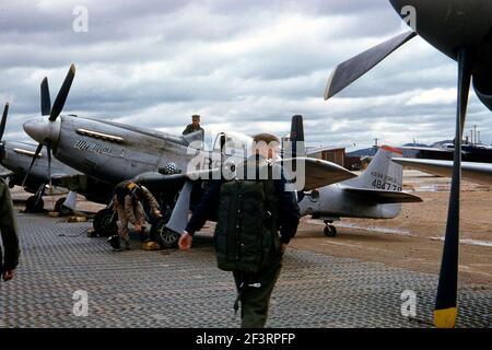 Ein Viertel linke Seitenansicht einer nordamerikanischen RF-51D 'My Mimi' (s/n 44-84778; c/n 44634), die irgendwo in Korea in der Fluglinie geparkt ist. Dem Piloten wird gezeigt, wie er in Richtung des Flugzeugs geht, und sein Helm sitzt auf dem linken Flügel. Ein Besatzungsmacht steht auf dem rechten Flügel neben dem Cockpit, und ein weiterer beugt sich neben dem linken Rad. Der Propeller eines anderen RF-51D Mustang ist auf der rechten Seite des Bildes zu sehen, und zwei weitere erscheinen auf der linken Seite. Im Hintergrund ist ein Douglas B-26B Invader Stockfoto