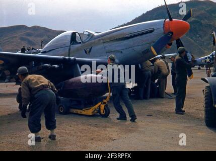 Ein Viertel rechte Seitenansicht eines nordamerikanischen Mustang Mk. IVA 'Patsy Dawn' (s/n KM366) wird irgendwo in Korea mit Falltanks ausgestattet. Zwei Männer bewegen den Falltank in Position unter dem rechten Flügel. Ein dritter Mann schaut auf. Drei Männer befestigen einen Falltank am linken Flügel. Ein anderer Mann steht vor der Nase des Flugzeugs, zwei weitere stehen am Ende des linken Flügels. Vor dem Flugzeug ist ein Jeep geparkt. Ein weiterer Mustang MK. IV und ein nordamerikanischer F-51D Mustang erscheinen im Hintergrund Stockfoto