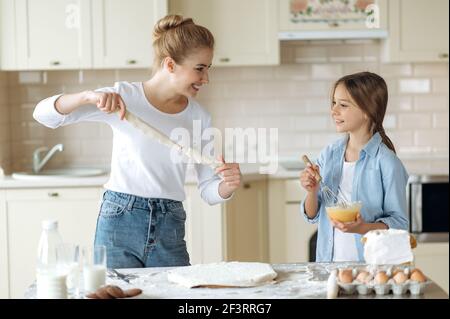 Glückliche junge Mutter und nette kleine Tochter Kochen zusammen in der Küche. Glückliche kaukasische Frau lehrt eine kleine Tochter zu kochen, verwenden Zutaten, sie glücklich verbringen Zeit zusammen Stockfoto