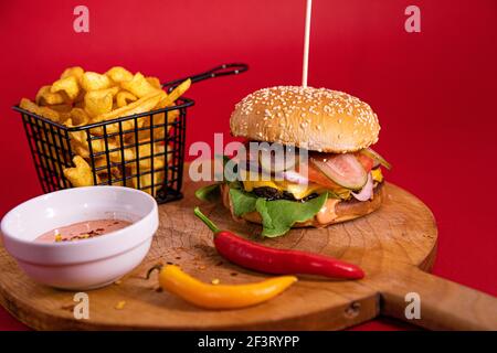 Ein großer Burger, pommes Frites, Fry Sauce und zwei Chilischoten auf einem Holzbrett serviert Stockfoto