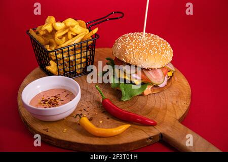 Ein großer Burger, pommes Frites, Fry Sauce und zwei Chilischoten auf einem Holzbrett serviert Stockfoto