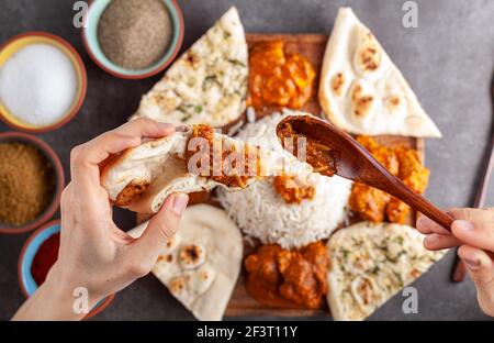 Flaches Lay-Bild einer Frau, die Huhn Tikka Masala auf eine Scheibe Naan-Brot mit einer Platte mit traditionellen indischen Speisen darunter. Gewürze und Kräuter Stockfoto