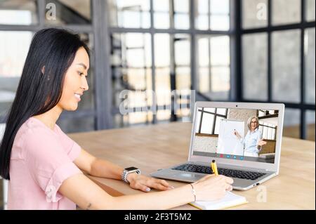 Junge asiatische Frau mit Anwendung für Fernvideokommunikation online über Laptop, einen virtuellen Kurs nehmen, von zu Hause aus studieren und Notizen machen, alte Dame Lehrer erklären Material auf Whiteboard Stockfoto