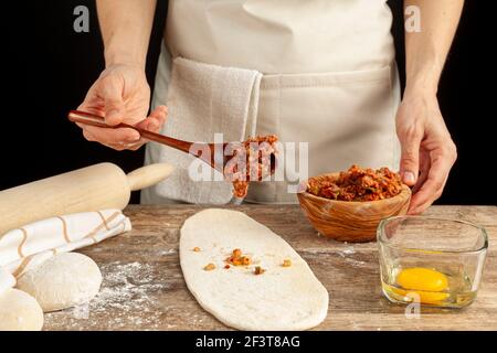 Eine Türkin bereitet Kiymali Pide, traditionelles Fladenbrot mit gemahlener Fleischpaste auf abgeflachten Teig zu und Eier werden auf der Mischung b verteilt Stockfoto