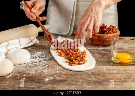 Eine Türkin bereitet Kiymali Pide, traditionelles Fladenbrot mit gemahlener Fleischpaste auf abgeflachten Teig zu und Eier werden auf der Mischung b verteilt Stockfoto