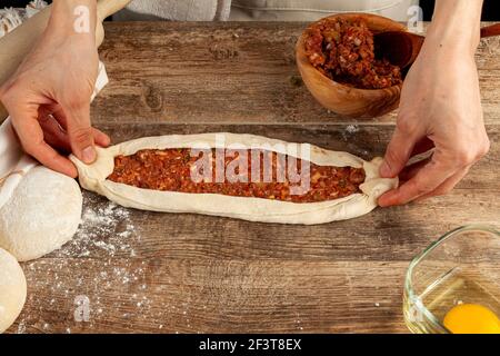 Eine Türkin bereitet Kiymali Pide, traditionelles Fladenbrot mit gemahlener Fleischpaste auf abgeflachten Teig zu und Eier werden auf der Mischung b verteilt Stockfoto