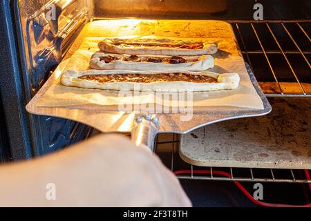 Traditionelle türkische Fladenbrote, bekannt als Kasarli suculu Pide und Kiymali Pide, werden auf heißem Stein gebacken. Ein großer Pizzaspatel legt sie auf h Stockfoto