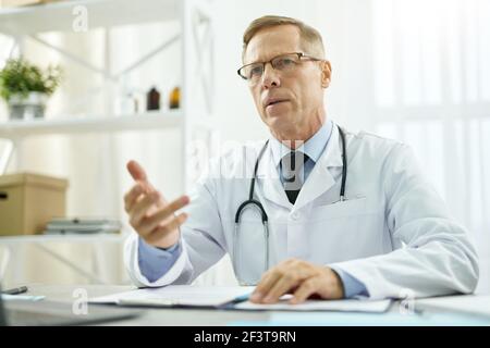 Hübscher Doktor, der am Tisch in seinem Büro sitzt Stockfoto