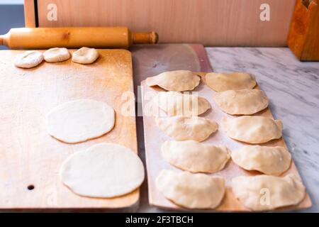 Kochend die Knödel mit den Kartoffeln, auf dem hölzernen Brett die Vorbereitung des Teiges, auf dem anderen Brett das fertige Produkt, die russische Küche Stockfoto