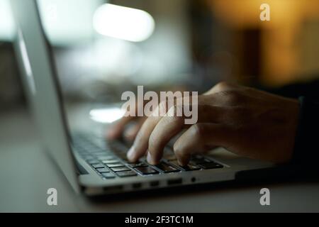 Prozess wird erstellt. Nahaufnahme der Hände eines jungen Mannes, der tippt, am Laptop arbeitet und spät in der Nacht am Tisch sitzt Stockfoto