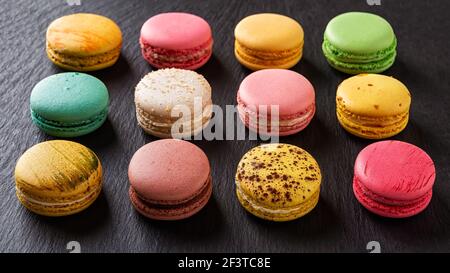 Set aus zwölf bunten Makronen auf schwarzem Hintergrund. Dutzende von bunten Macaron Kuchen Vielfalt. Köstliches französisches Dessert. Süßigkeiten aus Mandelmehl Stockfoto