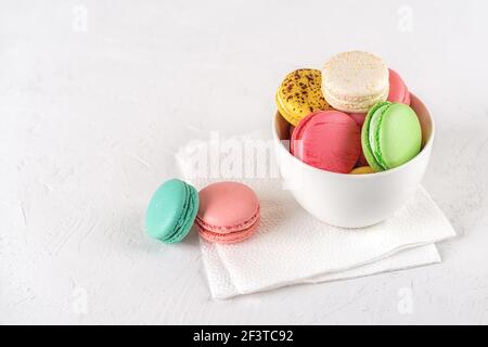 Bunte Makronen in einer weißen Keramikschale auf hellem Hintergrund. Bunte Macaron Kuchen Vielfalt. Köstliches französisches Dessert. Süßigkeiten aus Mandelmehl Stockfoto