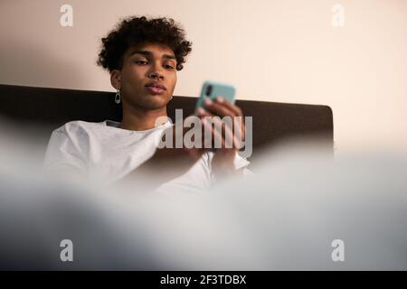 Beschäftigt junge Kerl mit Piercing mit Smartphone in seinem Bett In der Nacht vor dem Schlafengehen Stockfoto
