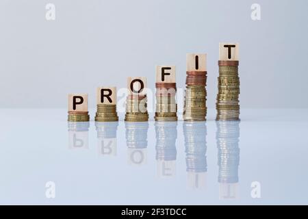 Wort "PROFIT" auf Holzblöcken auf aufsteigenden Münzstapeln auf Grau. Konzept Foto von Geld verdienen, Wirtschaft, Unternehmen, Finanzen und Erfolg. Stockfoto