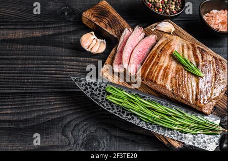 BBQ gegrillte Flanke oder Klappe Rindfleisch Steak auf einem Holzschneidebrett. Schwarzer Holzhintergrund. Draufsicht. Speicherplatz kopieren Stockfoto