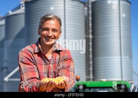 Farmer's Hands Holding Erntekorn. Glücklicher Bauer mit Maiskörnern in den Händen, der Kamera anschaut. Stockfoto