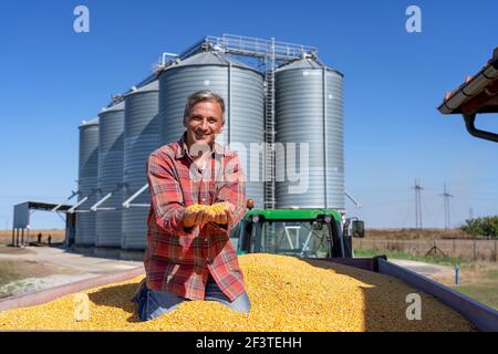 Farmer's Hands Holding Erntekorn. Glücklicher Bauer mit Maiskörnern in den Händen, der Kamera anschaut. Stockfoto