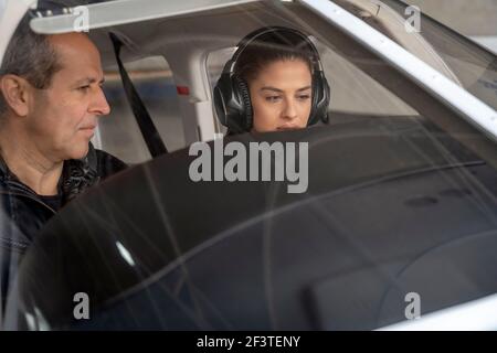 Porträt einer attraktiven jungen Frau Trainee Pilot mit Headset Vorbereitung auf den Flug. Sie sitzt neben dem Fluglehrer und schaut auf das Armaturenbrett. Stockfoto