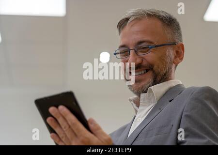 Handsome Reifen Geschäftsmann Holding Handy oder Digital Tablet. Lächelnder Business Executive mit digitalem Tablet im Büro. Stockfoto