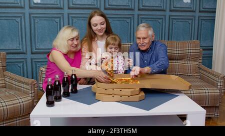 Glückliche Familie mit mehreren Generationen, die zu Hause eine Mittagsparty macht, Pizza isst und gemeinsam Toast macht Stockfoto