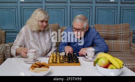Rentnerehepaar reden Tee trinken, spielen Schach in modernen Wohnzimmer Lounge zusammen Stockfoto