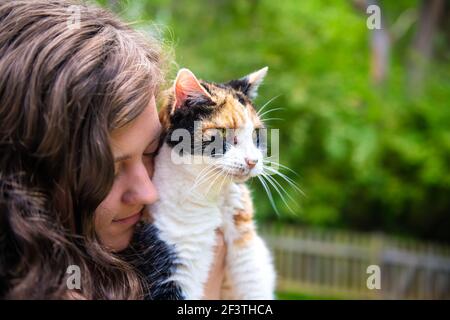 Nahaufnahme Porträt von glücklich lächelnd junge Frau Bonding halten in den Händen calico Katze Haustier Begleiter, stoßen reiben ammeling Köpfe, Freunde zeigen Wirkung Stockfoto