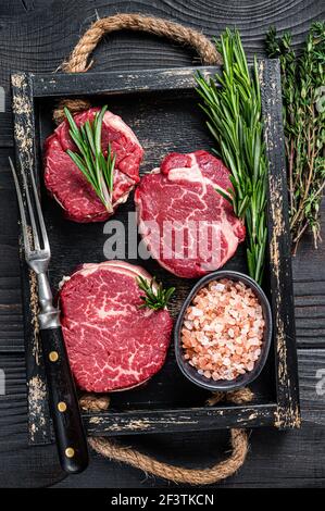 Filet Mignon Filet Roh Fleisch veak Steaks in Holzschale mit Kräutern. Schwarzer Holzhintergrund. Draufsicht Stockfoto